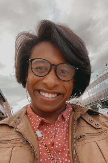 A woman with short dark hair wearing black glasses and a peach polka dot shirt
