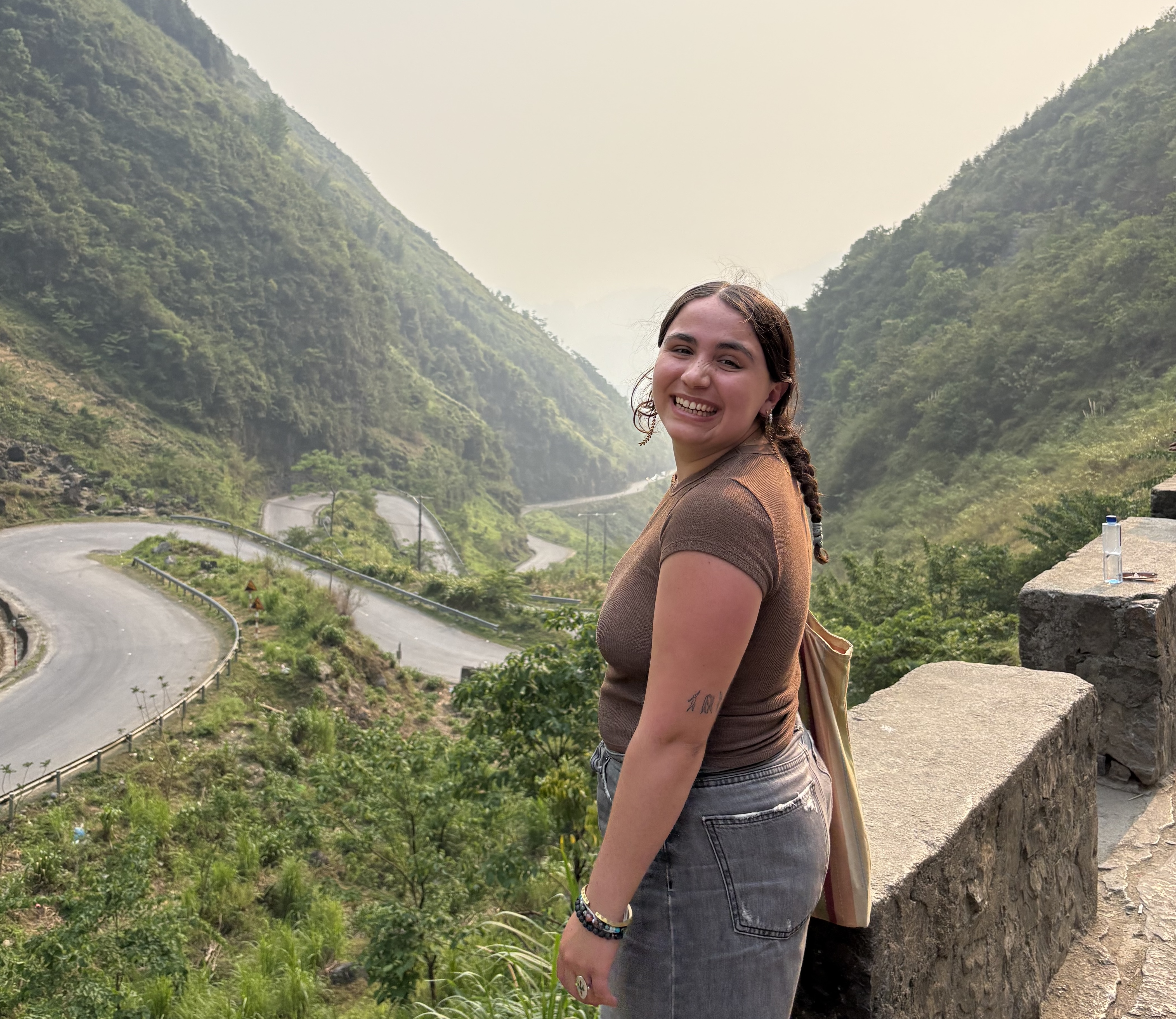 DU student Michela Schenk poses on a bridge overlooking green mountains.