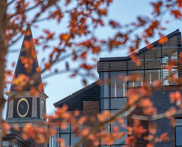 A landscape of the Burwell Center obscured by the red leaves of a tree in the foreground