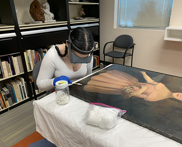 Emma Lynn Lehman cleans a painting using an enzymatic solution.