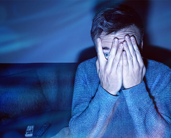 Frightened man watching movie through his fingers