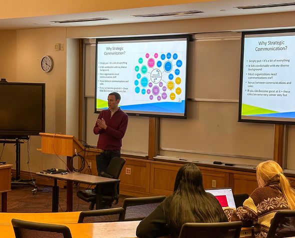 alumnus derek dash stands in front of a powerpoint presentation