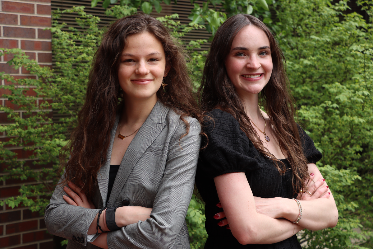 Two girls smiling & standing back to back