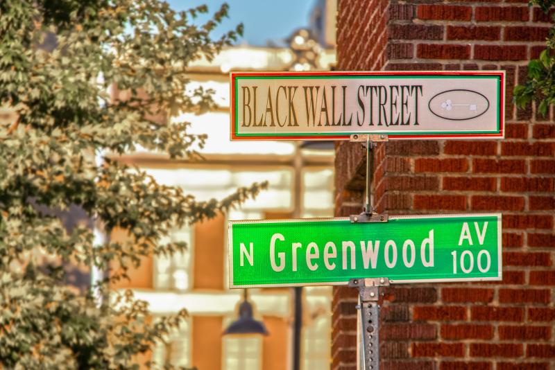 Two street signs, one that reads Black Wall Street, and the other that reads Greenwood.