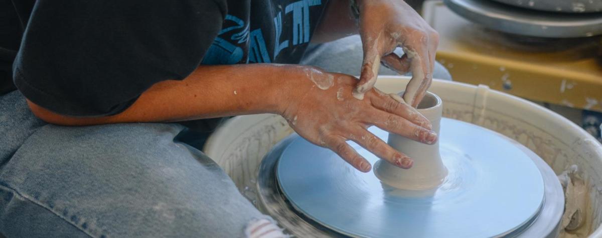 Student shapes clay on a potter's wheel