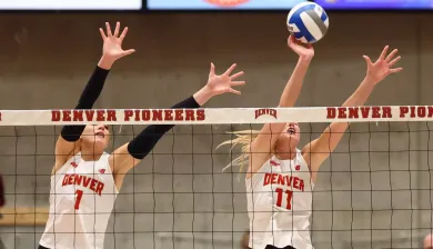 Two female volleyball players block at the net.