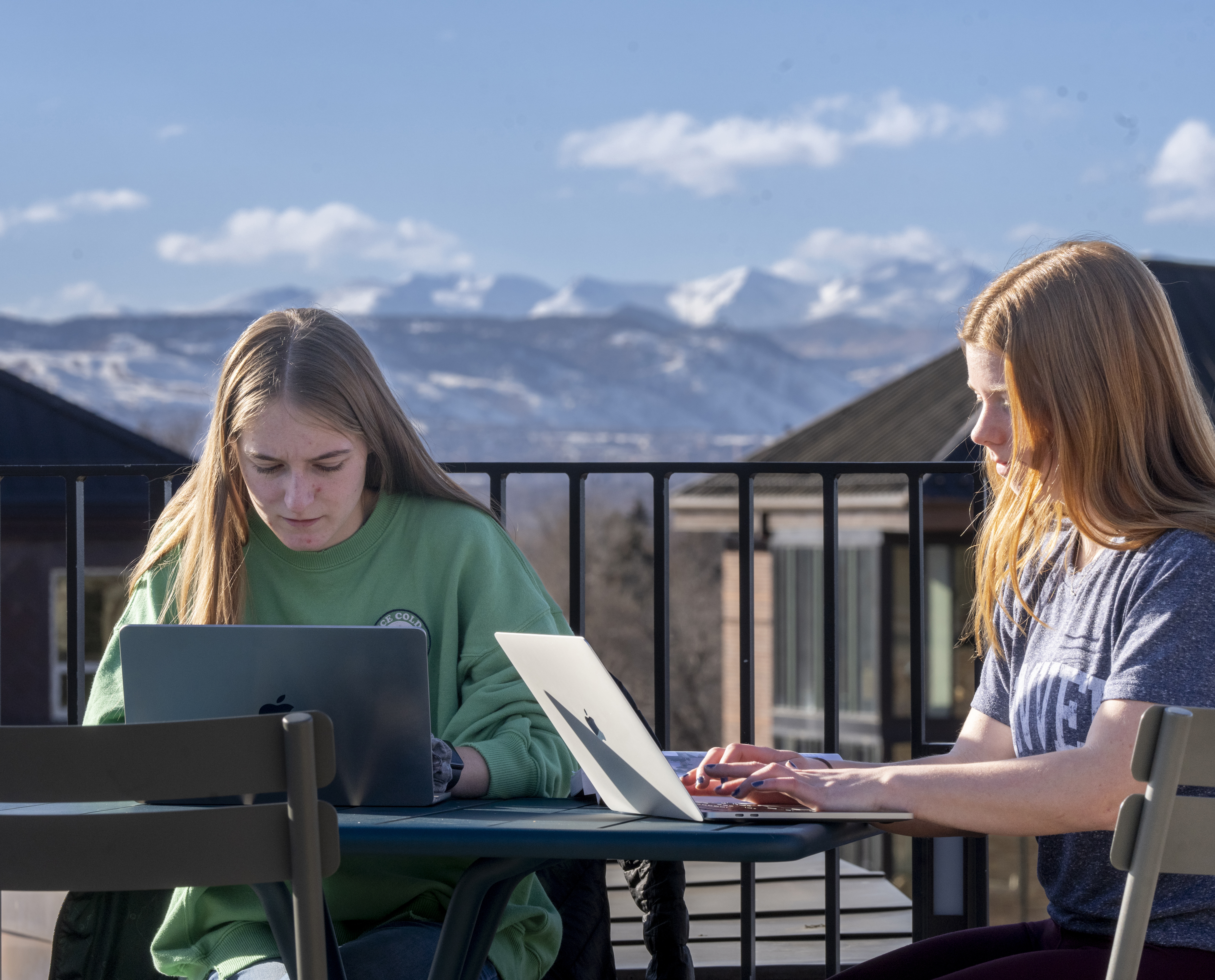 Two female students working on their laptops outdoors on the roof of the Community Commons.