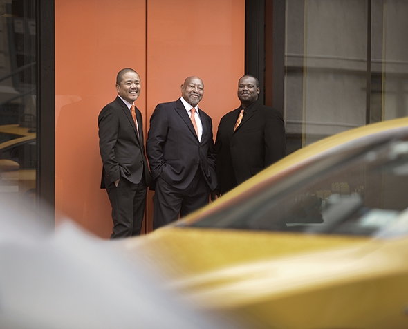 The Kenny Barron Trio stands against a wall with rushing traffic blurred in the foreground.