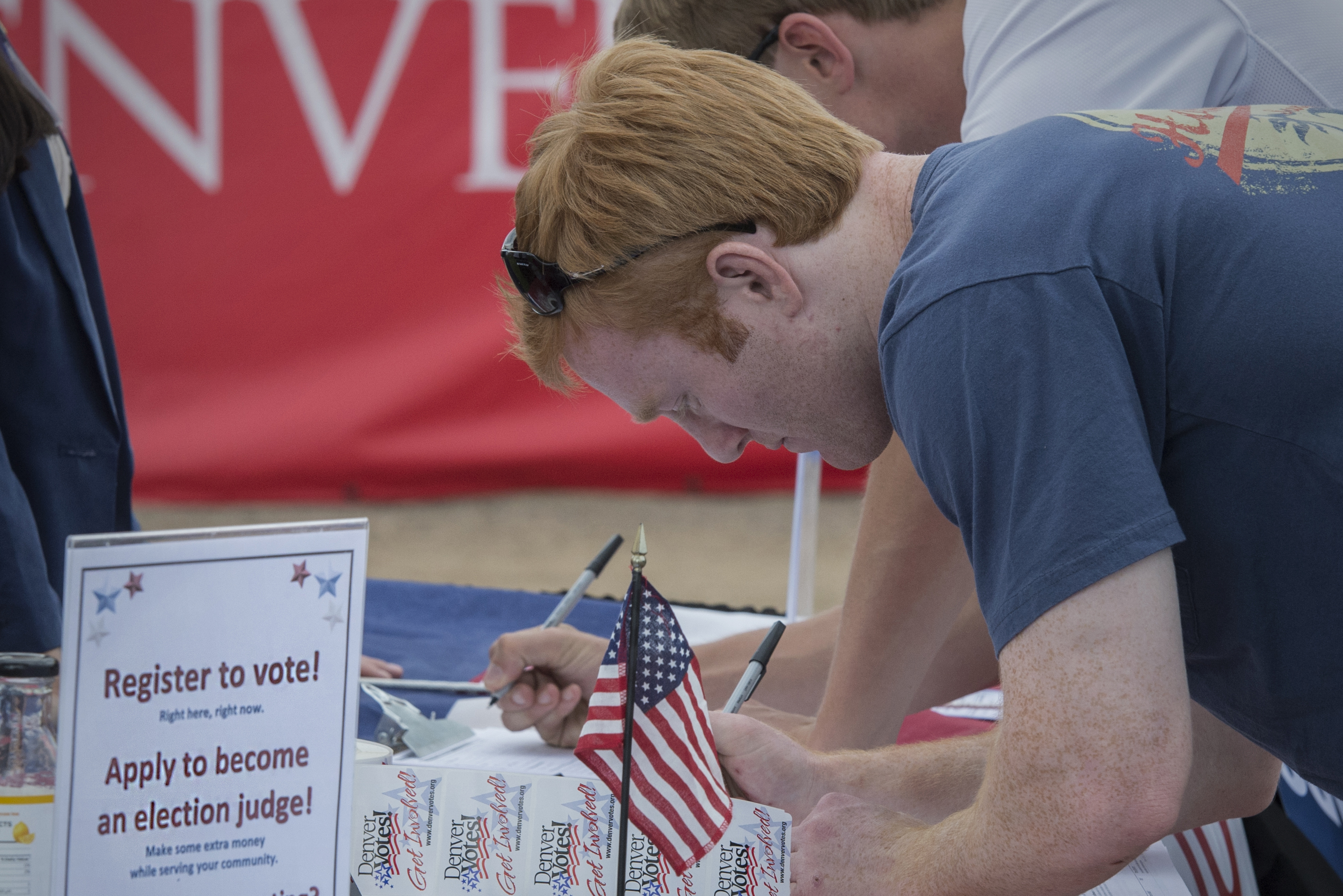 A young man registers to vote at a table with an american flag on it.
